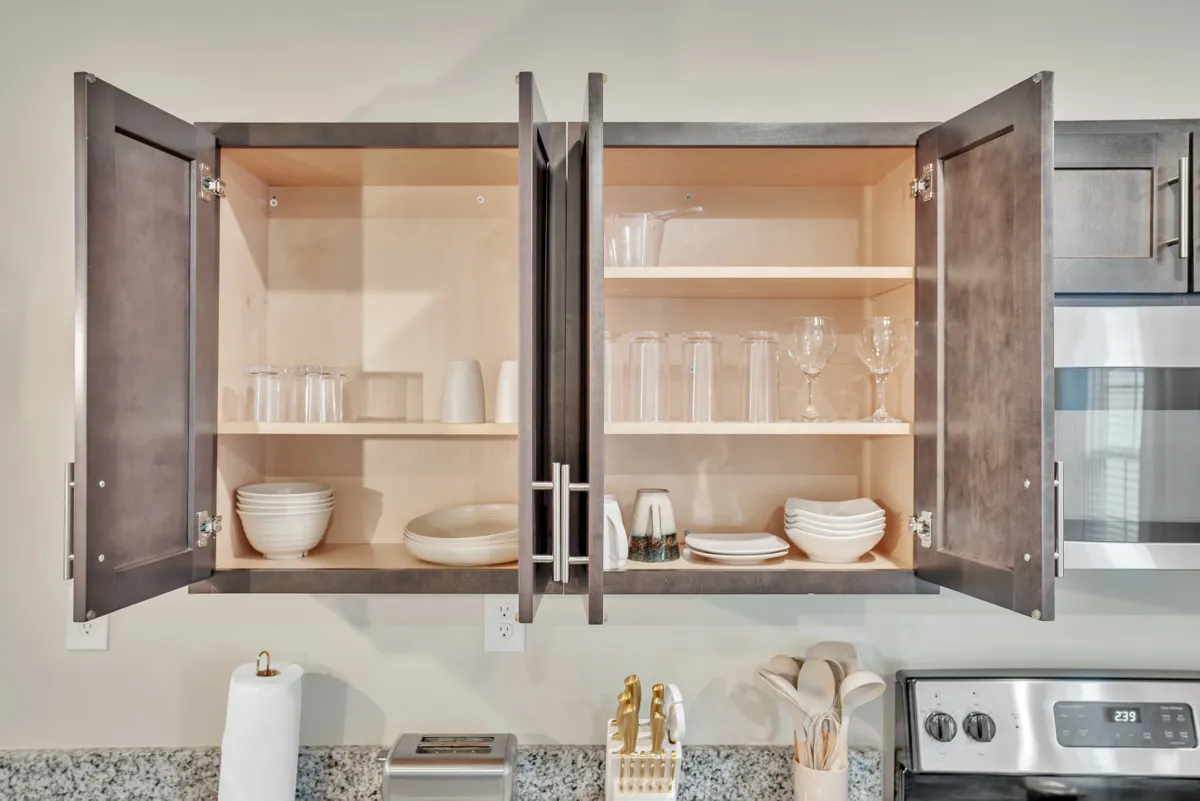 The photo showcases a well-appointed kitchen with open cabinets revealing glassware, plates, and utensils. The modern and welcoming setup is ideal for casual dining or preparing a meal after a long day.