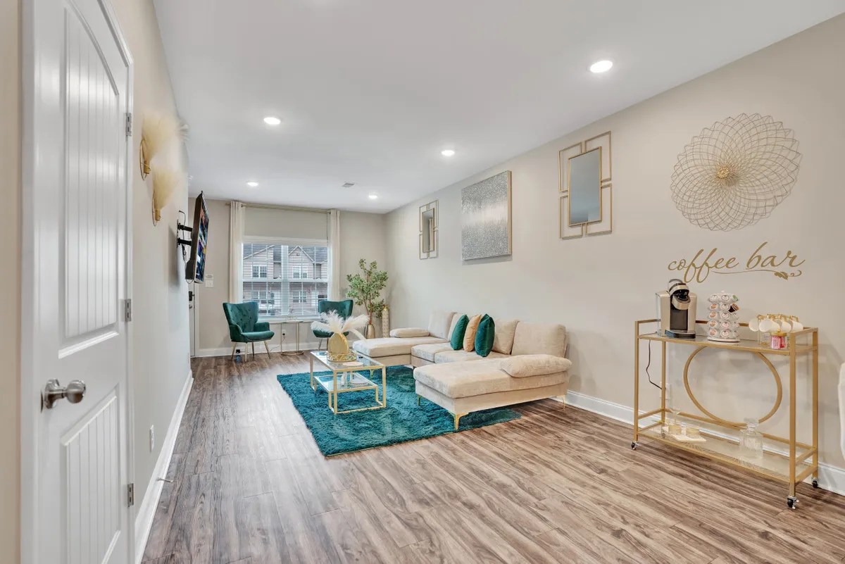 A comfortable lounge area with a soft sofa, a convenient coffee bar setup, decorative mirrors, and green accessories. The space is designed for both socializing and quiet moments, with a cozy, welcoming vibe.