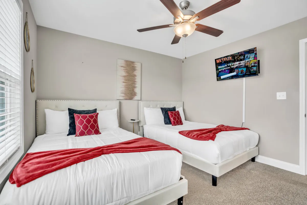 The image features two inviting beds topped with decorative pillows, a wall-mounted TV, and a stylish ambiance that suggests both comfort and versatility. The arrangement of the beds and the presence of entertainment options highlight the space’s suitability for different types of guests and activities.