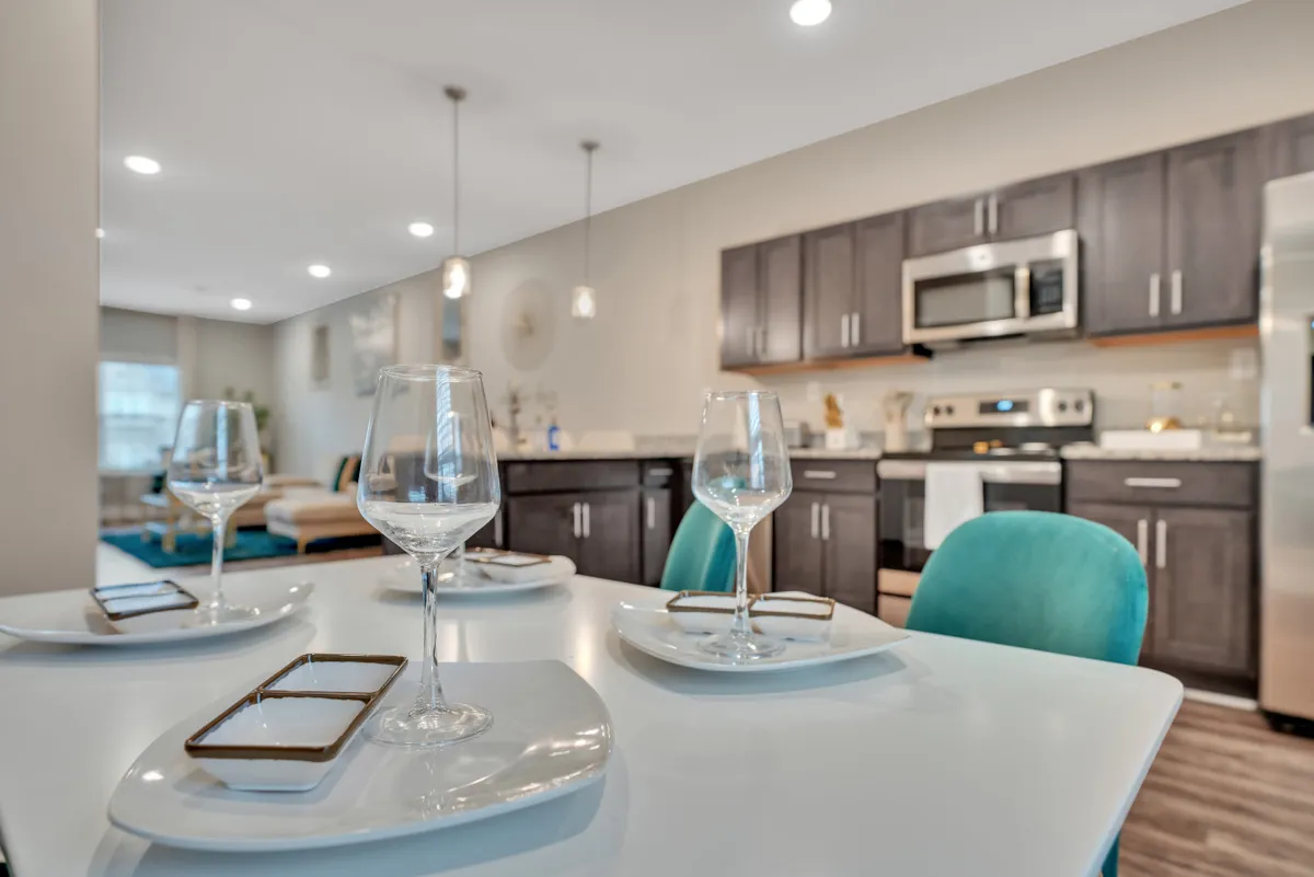 A dining area adjacent to the kitchen, featuring glassware, dinnerware, and cabinetry that hints at an upcoming meal or gathering. The setting is inviting, with enough visual detail to suggest both intimacy and the potential for celebration.
