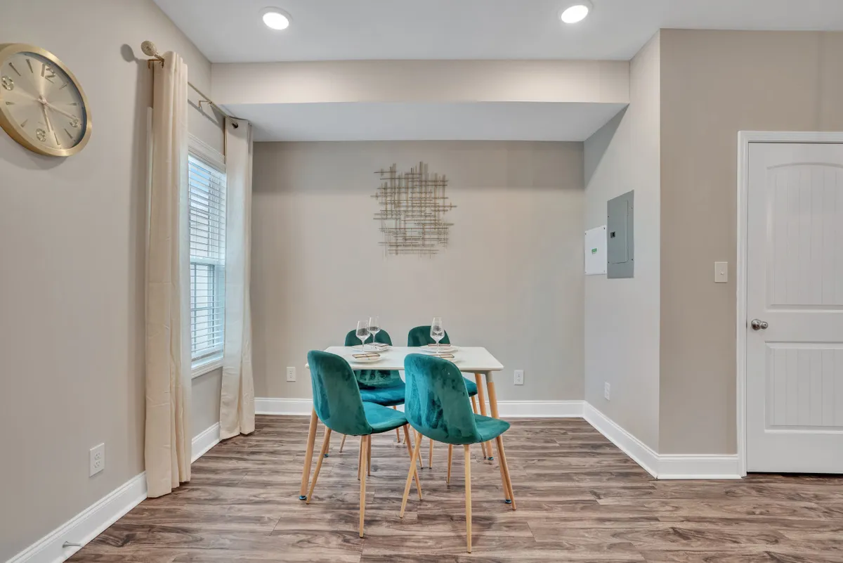 An open dining and work area with a modern table surrounded by blue-green chairs, highlighted by bold wall art and a decorative clock. The setting is ideal for casual dining, working, or brainstorming with colleagues.