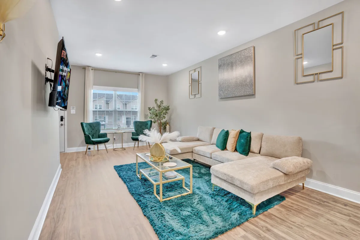 The image showcases a stylish, sunlit living room with a plush sofa, elegant coffee table, tasteful area rug, and decorative mirrors, creating a warm and welcoming space ideal for relaxation and social gatherings.