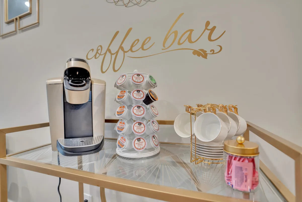 A cozy countertop coffee station with a coffee maker, coffee pod holder, white cups, and a decorative jar. The setup exudes a welcoming, homey vibe ideal for starting the morning or enjoying a coffee break.