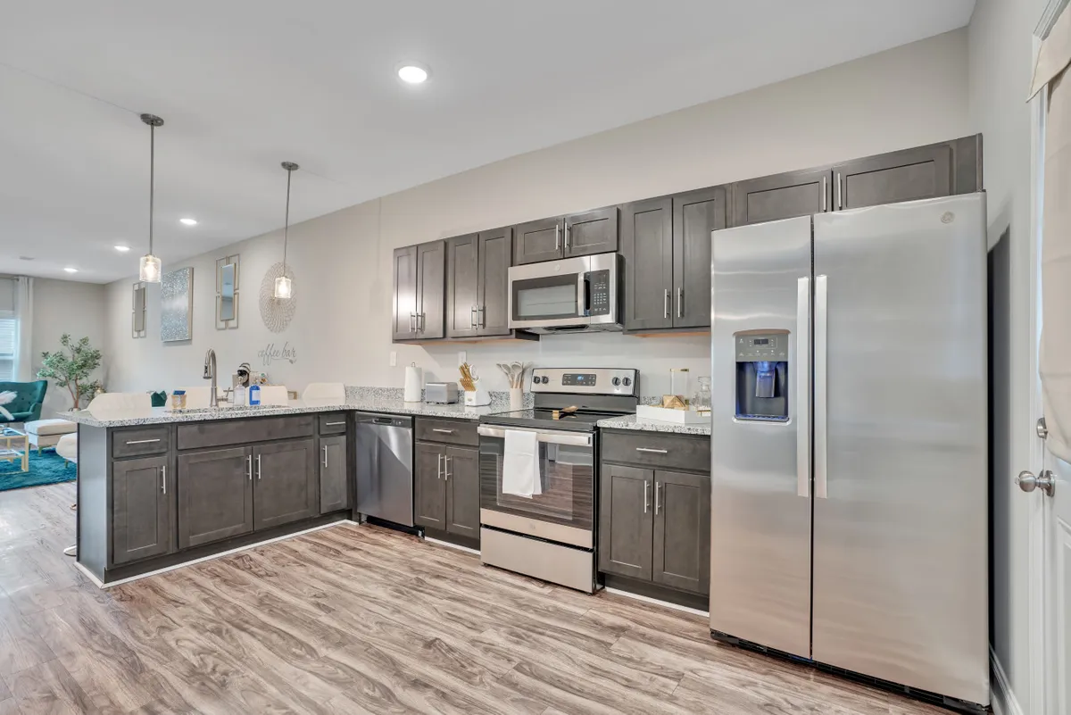 A cozy kitchen scene centered around a large island, flanked by stainless steel appliances and expansive granite countertops. The atmosphere is warm and welcoming, ideal for group cooking sessions, family dinners, or social gatherings around the island.