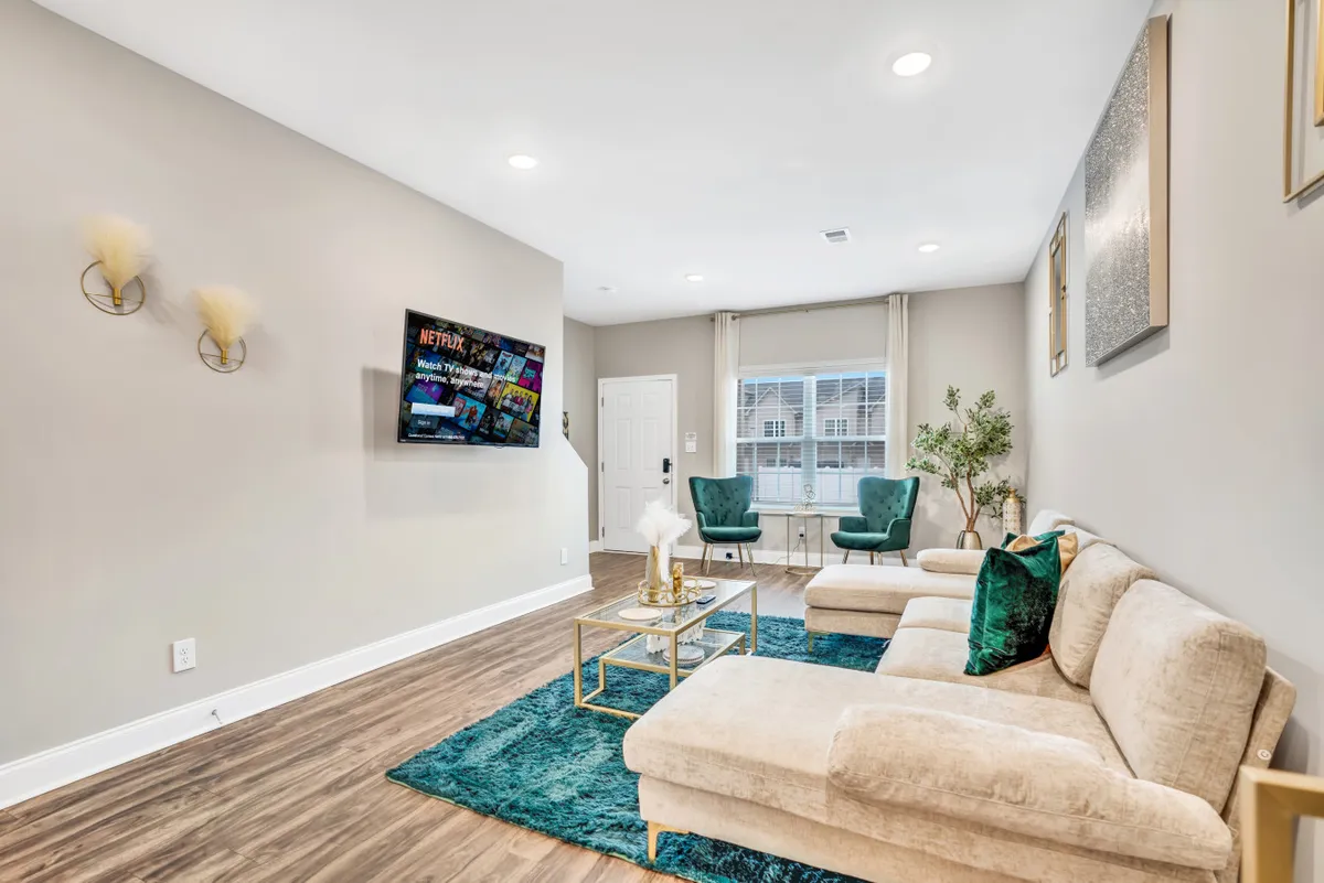 A stylish living room featuring a cozy sofa, a TV, a chic coffee table, green accent chairs, and a large window with flowing curtains. The overall look is modern yet inviting, perfect for relaxation, socializing, or unwinding after a busy day.